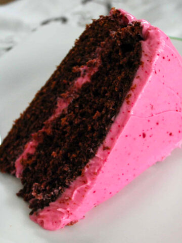 A slice of chocolate beet cake with cream cheese beet frosting on a plate next to a fork.