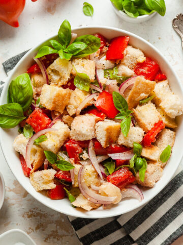 a bowl of panzanella salad with a striped napkin and herbs