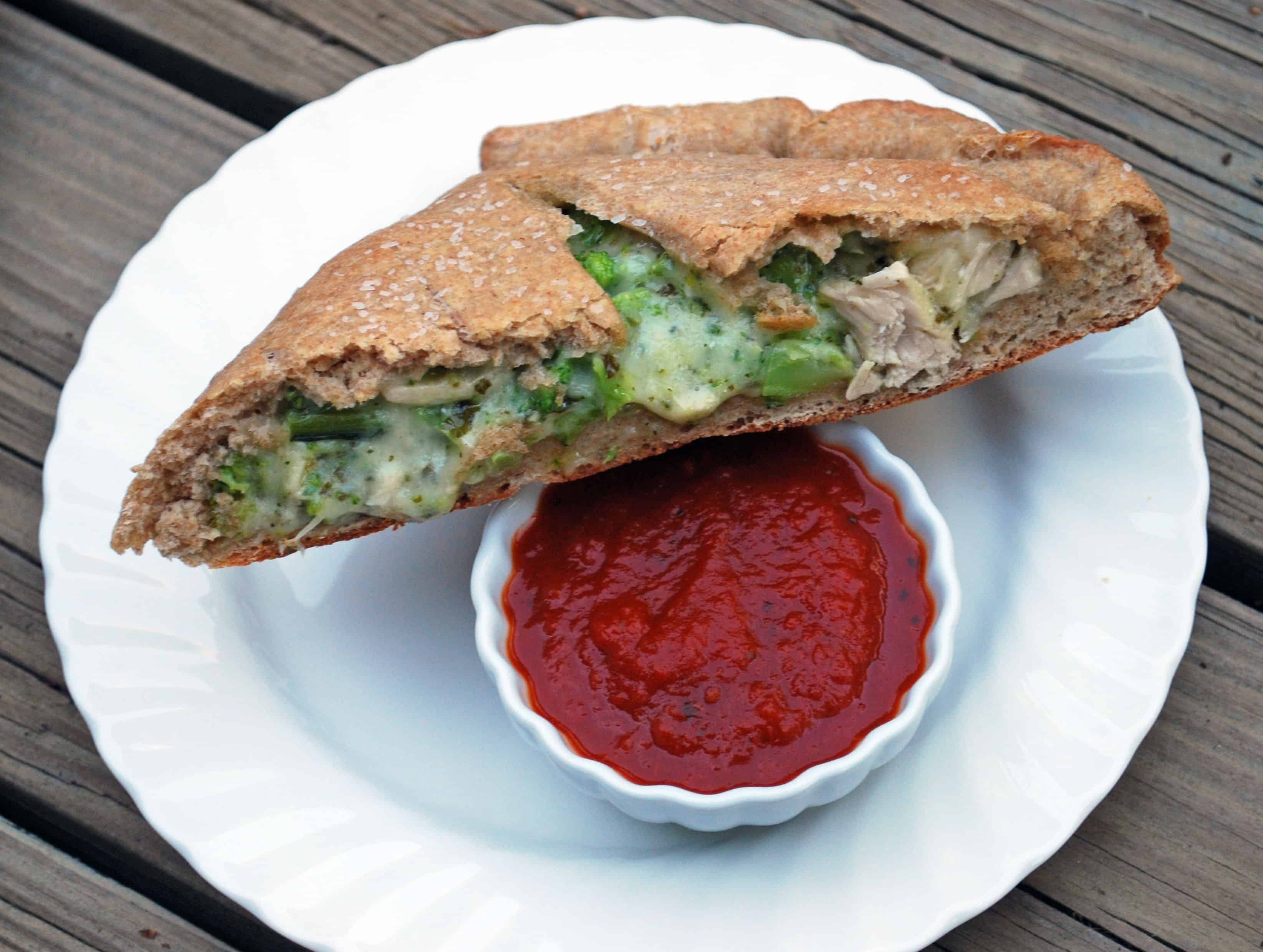 Chicken and Broccoli Calzone a slice of Chicken and Broccoli Calzone on a white plate next to a small bowl of marinara sauce