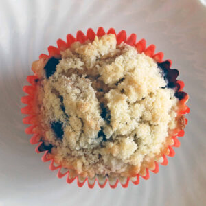 overhead view of a brown butter blueberry muffin in a red wrapper on a white plate