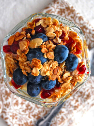Blueberry pomegranate breakfast parfait in a glass next to a spoon.