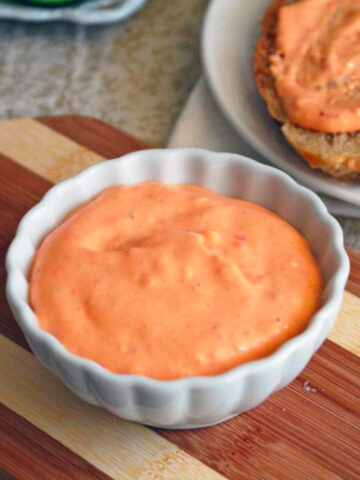 Roasted Red Pepper Whipped Goat Cheese in a small white dish on a wooden cutting board.