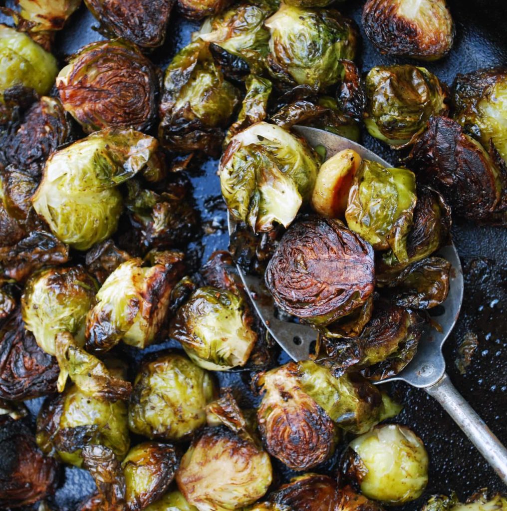 a metal spoon scooping up balsamic roasted brussels sprouts with garlic