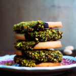 side view image of five pistachio and chocolate dipped cookies on red and white plate.