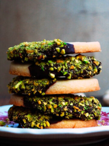 side view image of five pistachio and chocolate dipped cookies on red and white plate.