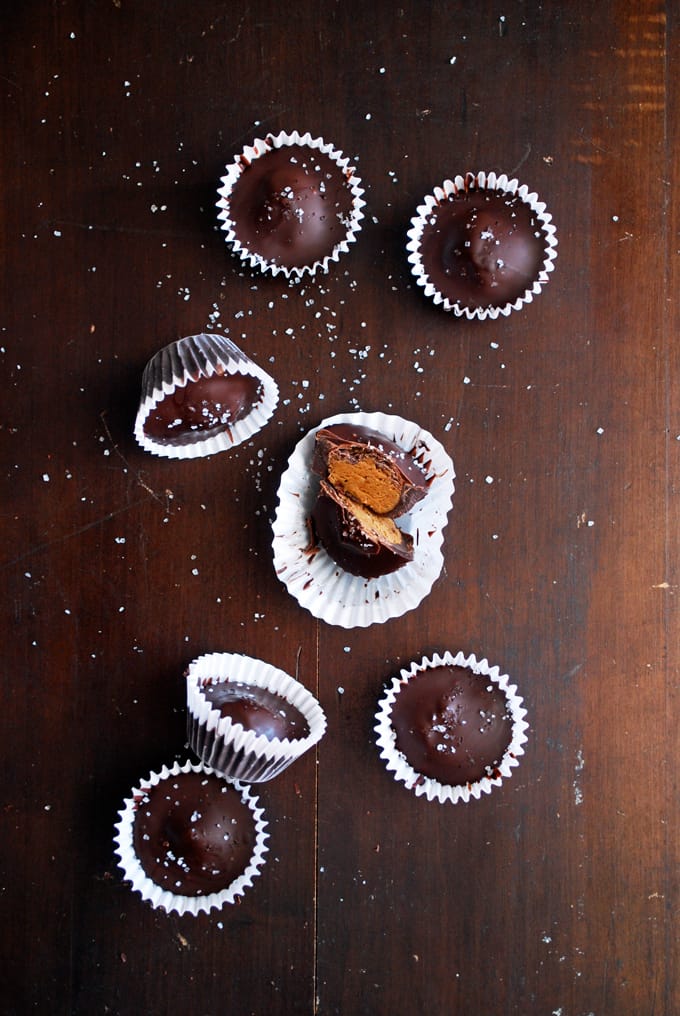 several dark chocolate almond butter cups on a wood table, one cut in half