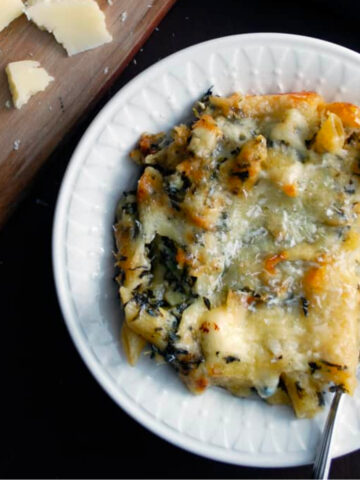 a bowl of spinach artichoke mac and cheese with parmesan and a grater