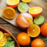a glass of rum punch on a wood table with cut limes and oranges