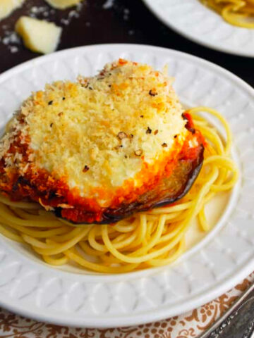 plates with eggplant parmesan and block of parmesan cheese on table