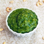 Homemade pesto in a dish with pine nuts scattered all around.