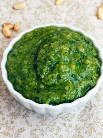Homemade pesto in a dish with pine nuts scattered all around.