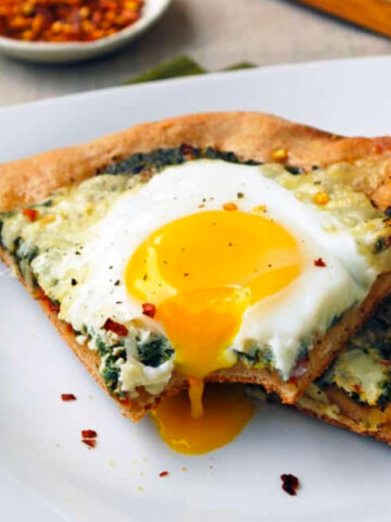 a slice of spinach and egg pizza with a dripping egg yolk.