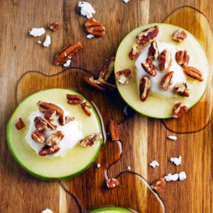 two apple slices with goat cheese, honey, and pecans on a wood cutting board