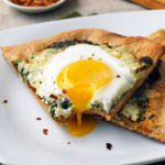 a slice of spinach and egg pizza with a dripping egg yolk