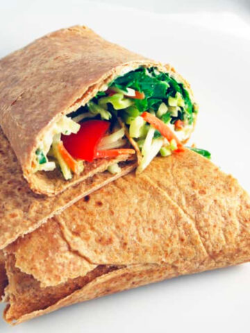 a white bean hummus and veggie wrap cut in half on a white plate.