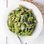 spinach pesto pasta in a white bowl with a fork and napkin