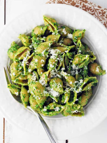 spinach pesto pasta in a white bowl with a fork and napkin