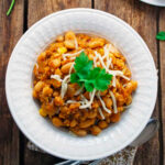 a white bowl of vegetarian quinoa white chili on a wood table.