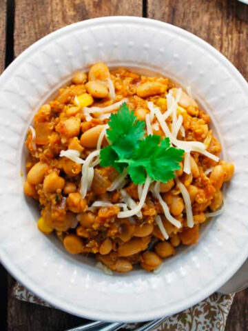 a white bowl of vegetarian quinoa white chili on a wood table.