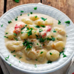creamy crab gnocchi in a white bowl on a napkin and wood table with a fork and parsley.