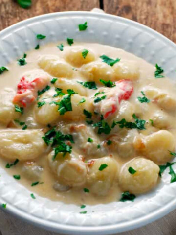 creamy crab gnocchi in a white bowl on a napkin and wood table with a fork and parsley.