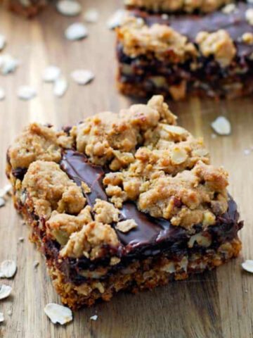 three chocolate oat bars with oatmeal on a wood cutting board