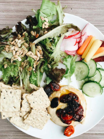 Vegetables, crackers, and hummus on a plate.