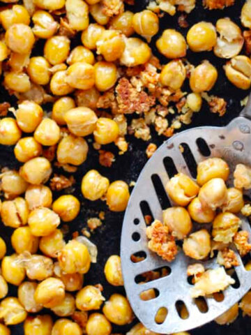 close up of roasted chickpeas in a pan with a slotted spoon