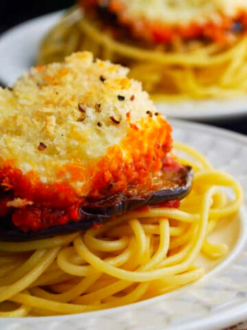 Two plates of eggplant parmesan on spaghetti.