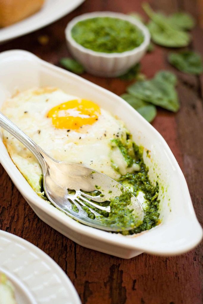 a baking dish of spinach pesto baked eggs with a serving spoon