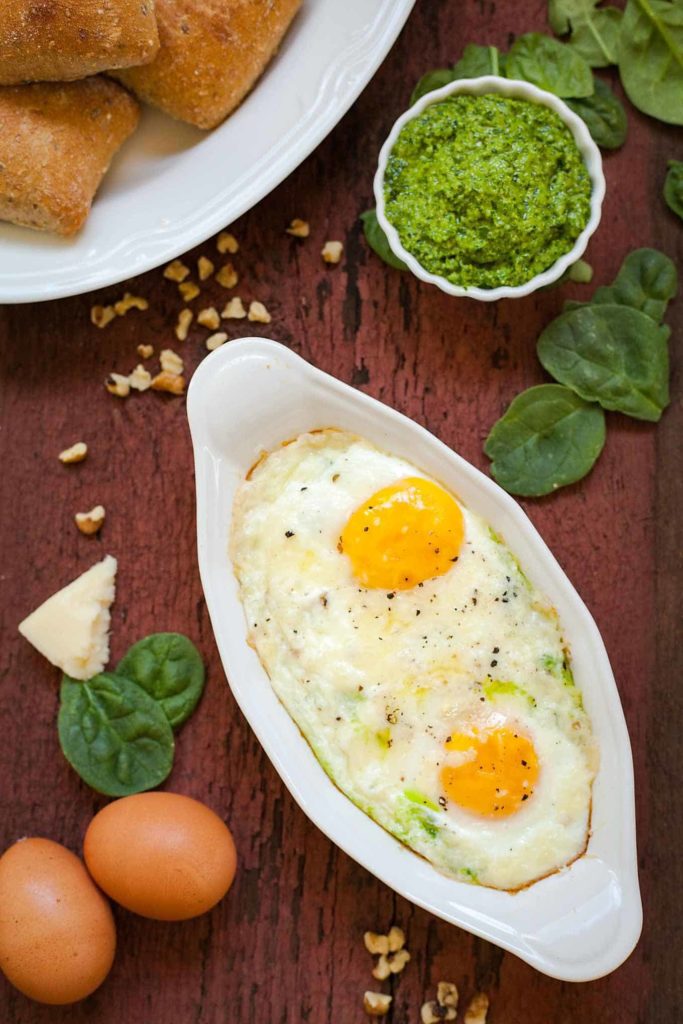 spinach pesto baked eggs on a wood table with eggs, spinach, pesto, and walnuts