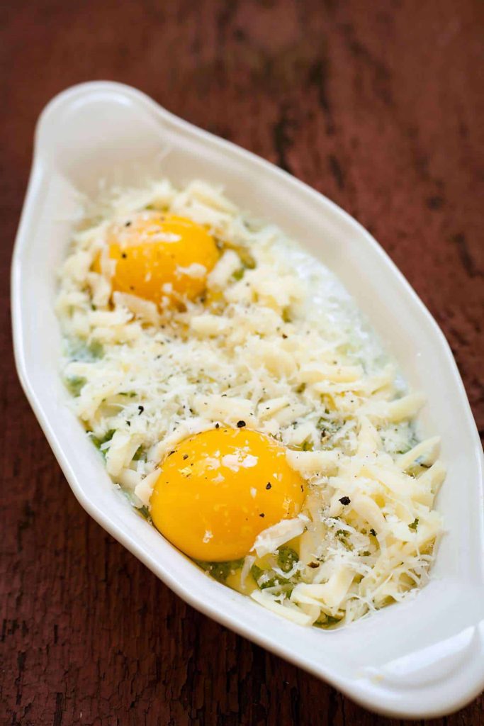 pesto, eggs, and cheese in a baking dish before being baked