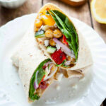 a greek chickpea wrap cut in half on a plate.