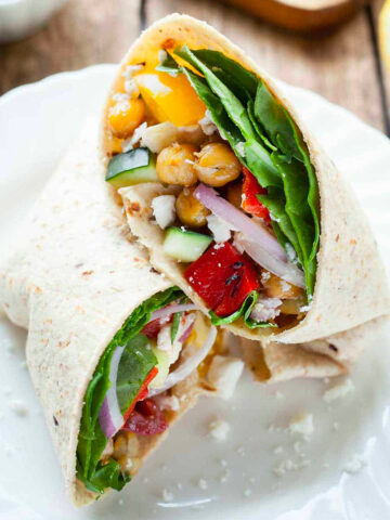 a greek chickpea wrap cut in half on a plate.
