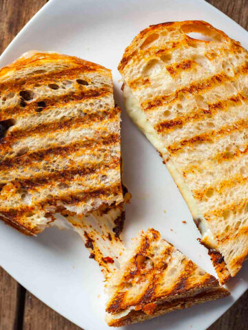 a harissa grilled cheese sandwich cut in half on a white plate.