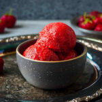 three scoops of strawberry sorbet in a small bowl on a platter.