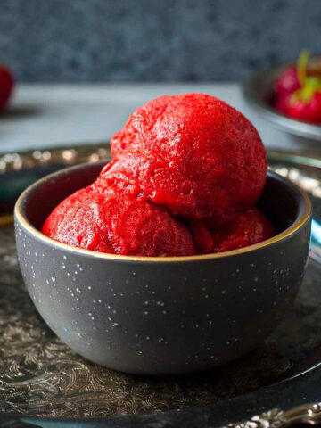 three scoops of strawberry sorbet in a small bowl on a platter.