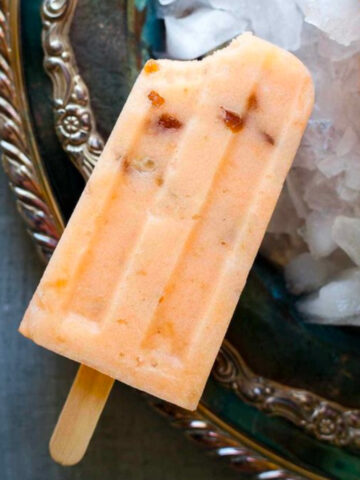 a cantaloupe popsicle with a bite taken out of it on a platter of ice.