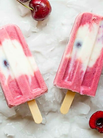 frozen yogurt popsicles laid out on ice with cherries.