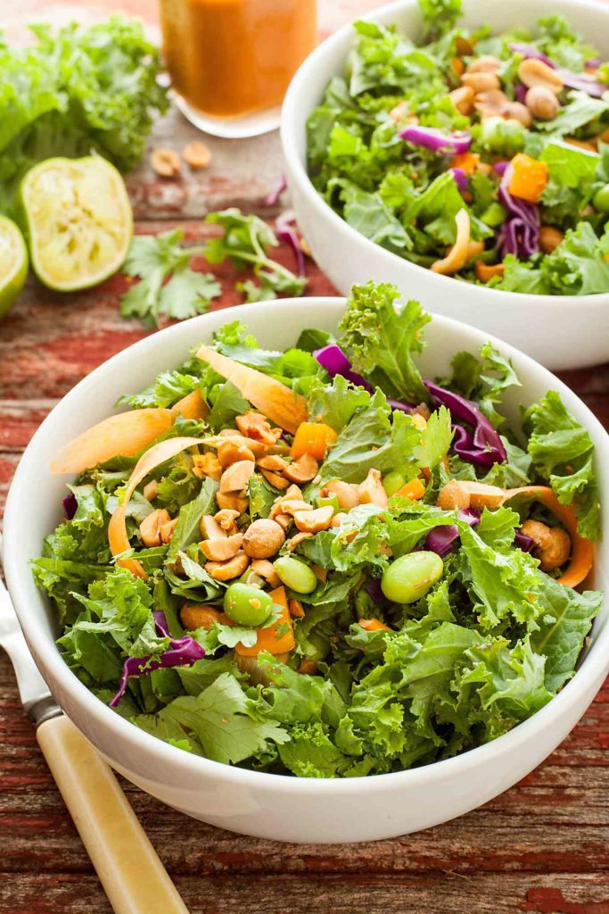 two bowls of healthy green salad with peanut butter dressing