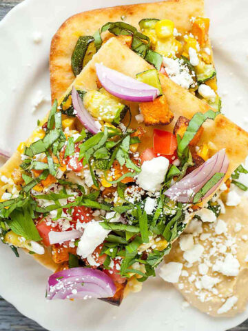 two slices of rainbow feta flatbread on a white plate with hummus