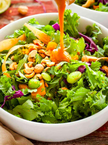 a bowl of healthy green salad topped with peanuts and dressing.