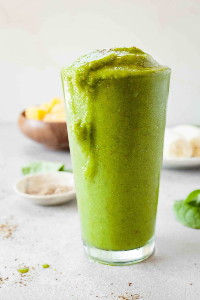 side image of tropical green smoothie with some spilling over and ingredients in background