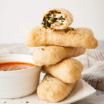 a stack of spanakopita pizza dippers next to a bowl of marinara sauce