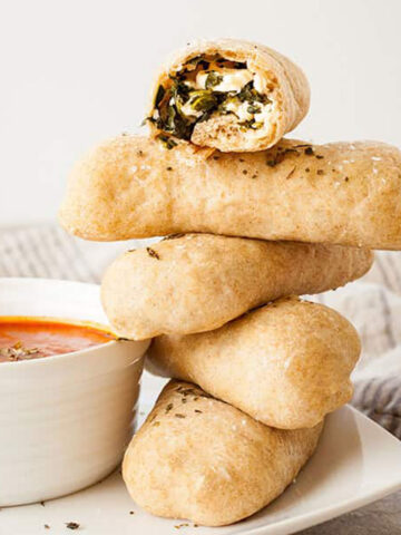 a stack of spanakopita pizza dippers next to a bowl of marinara sauce