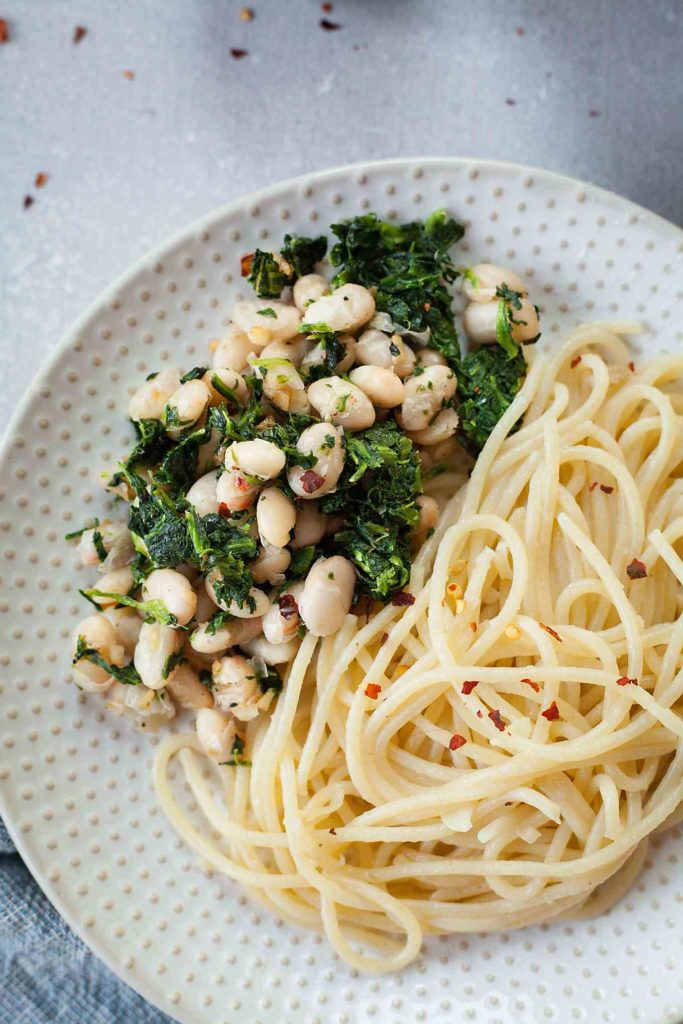 a polka dot plate with spaghetti, spinach, and white beans