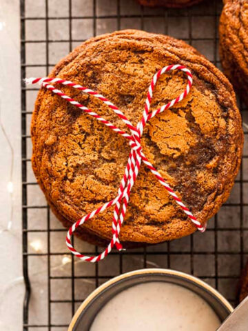 Giant ginger cookies wrapped in a white and red stripped bow next to a bowl of icing.