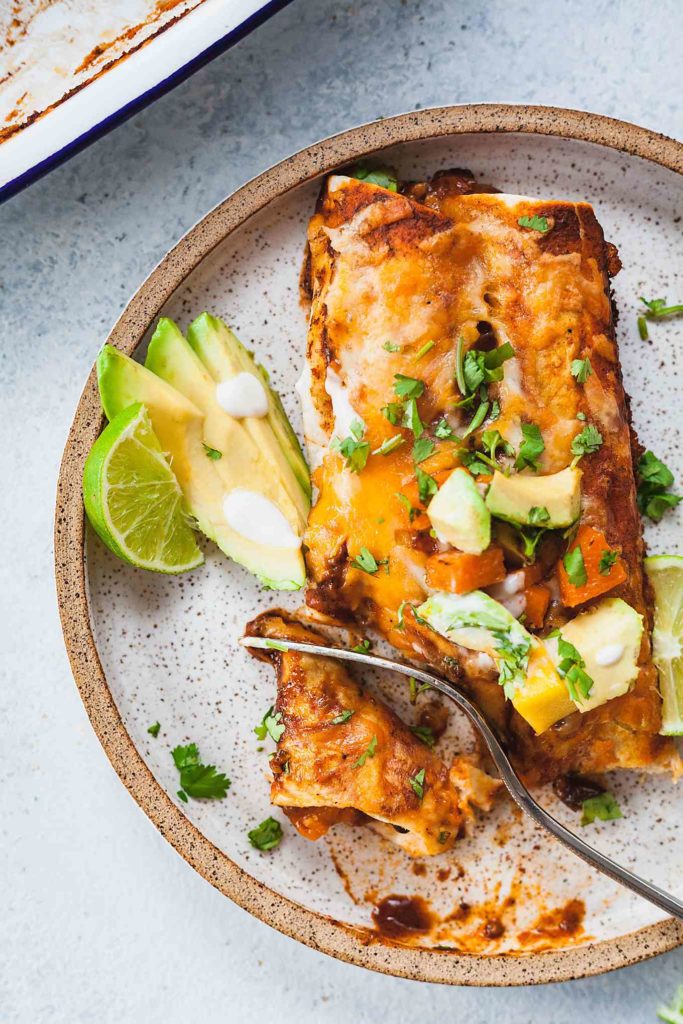 rustic plate with two butternut squash enchiladas being cut into with a fork