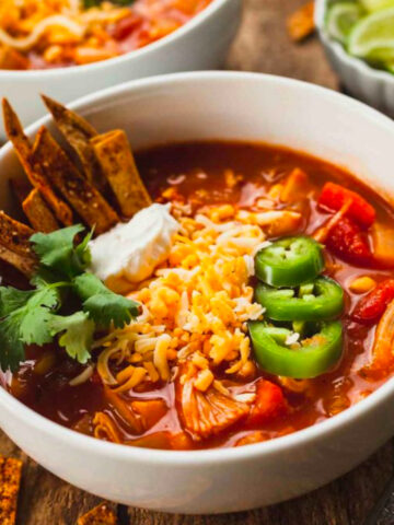 jackfruit tortilla soup in a bowl topped with sour cream, cheese, jalapeno, and tortilla strips.