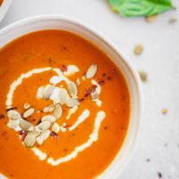 close up on tomato soup in a white bowl with basil and pepitas